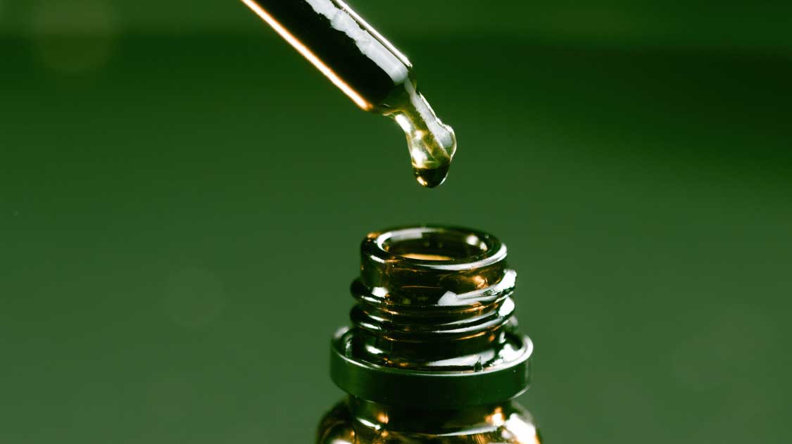 CBD oil bottle with dropper on green background